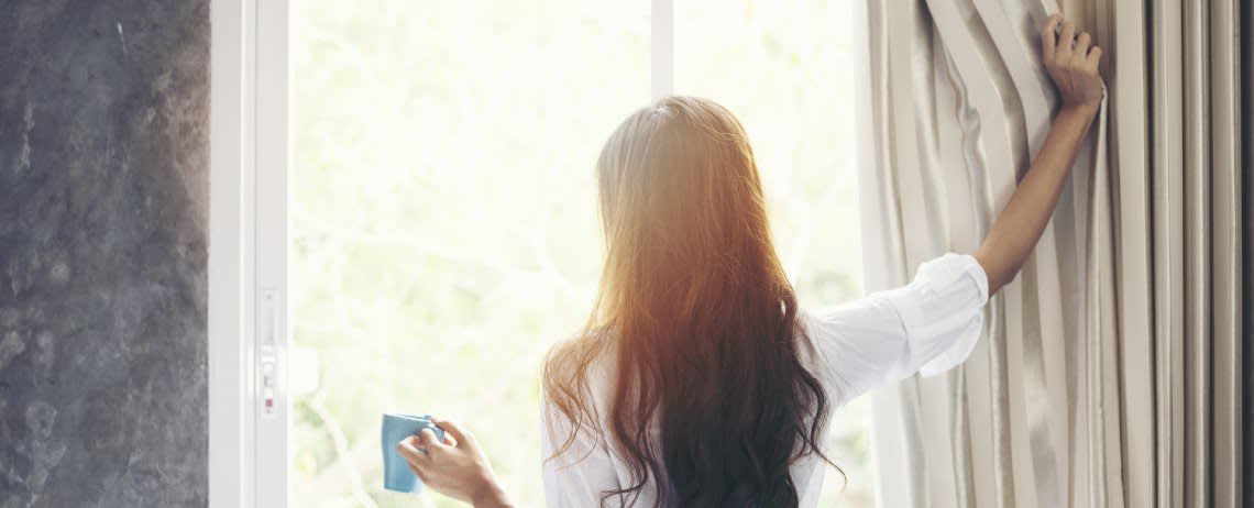 woman pulling back the a curtain to look outa window
