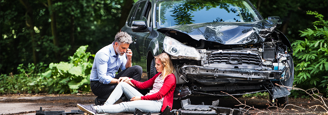 Young woman by the car after an accident and a man making a phone call