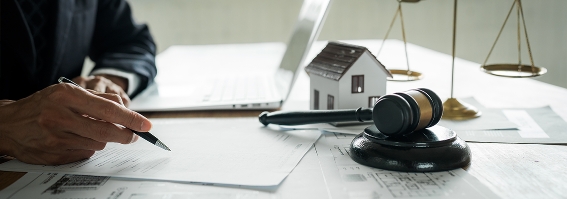 Real estate professional reviewing property documents at a desk with a house model, legal gavel, architectural plans
