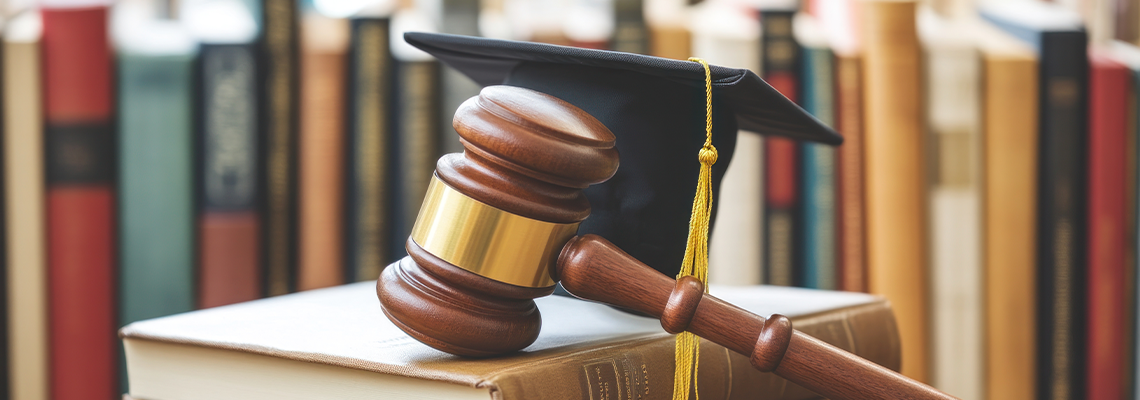 Graduation hat leaning on judge gavel resting on law books on desk