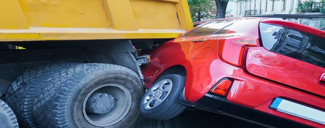 Small red car jammed underneath a large truck