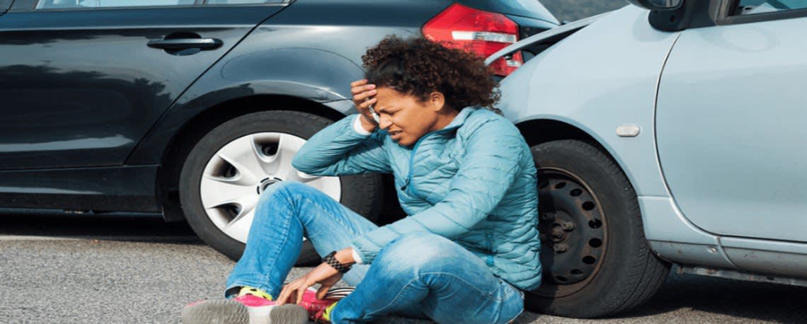 Woman distressed on the ground leaning against her car right after a fender bender