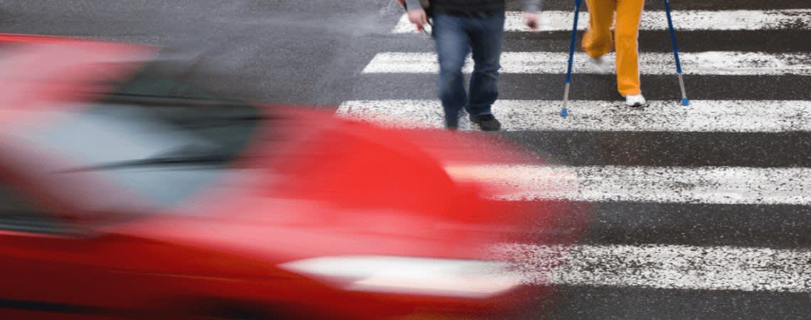 Two Pedestrians crossing a street while a car flashes by