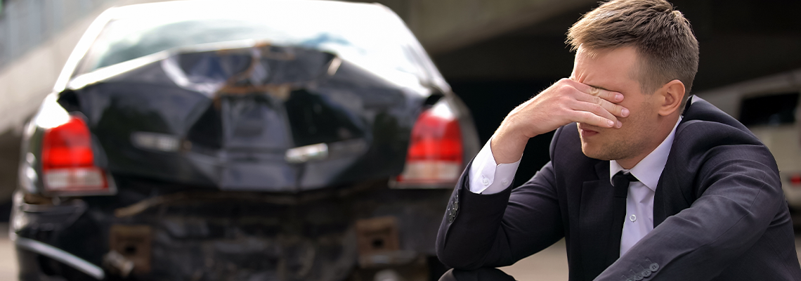 Desperate man sitting asphalt on crashed car background, automobile accident