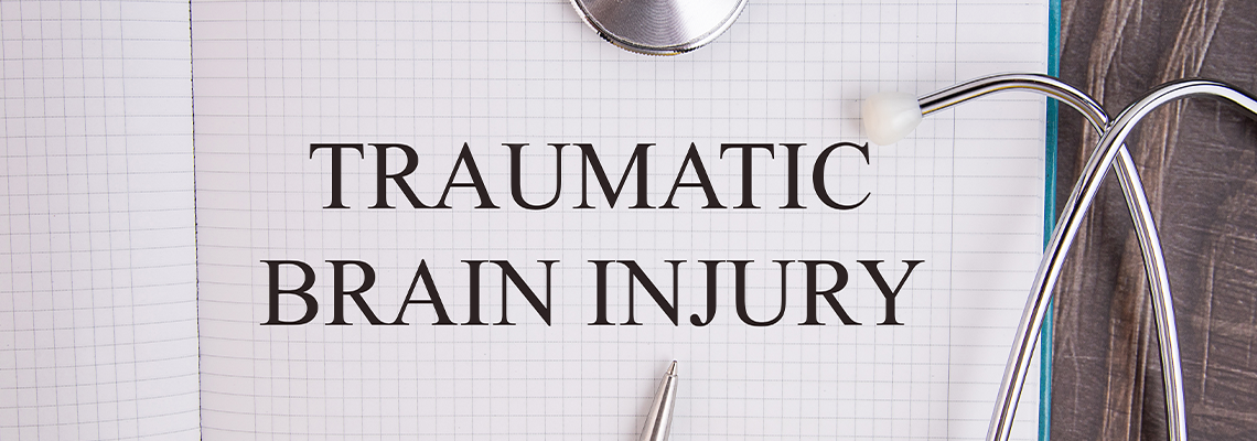 Notebook page with text TRAUMATIC BRAIN INJURY, on a table with a stethoscope and pen