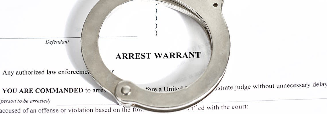 An arrest warrant document with handcuffs on top
