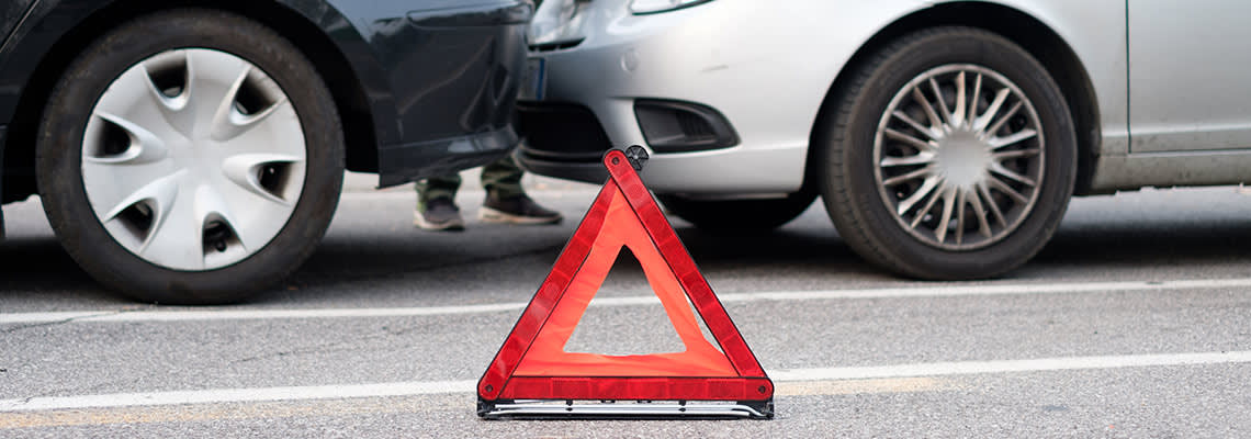 A hazard sign sits in front of two crashed cars