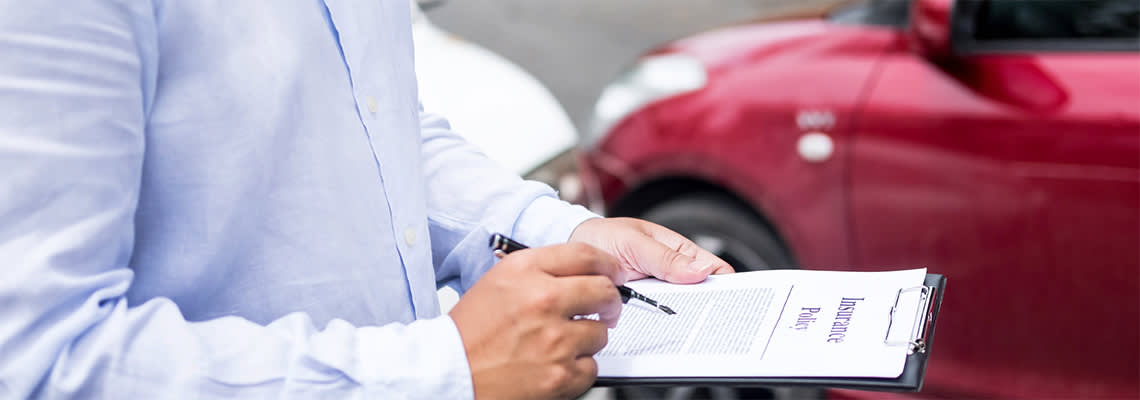 Insurance agent writing on clipboard while examining car after accident