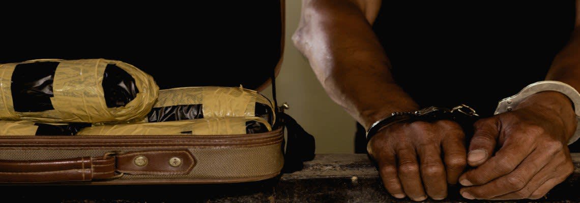 Handcuffed man next to suitcase full of drugs