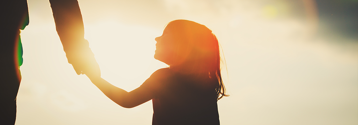 silhouette of little girl holding parent hand at sunset