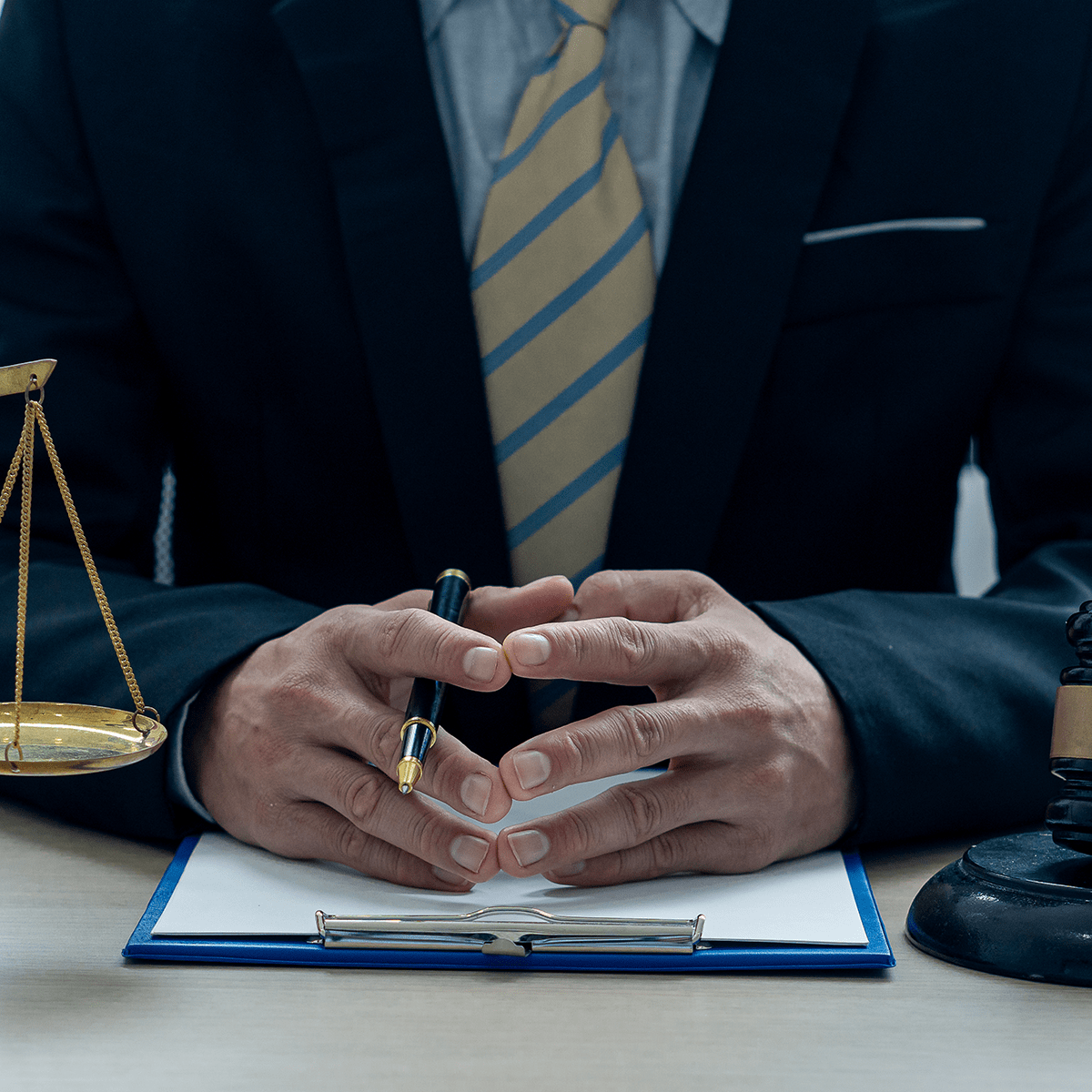 A lawyer or judge works in the office handing the paperwork with a hammer and scales of justice on closeup table