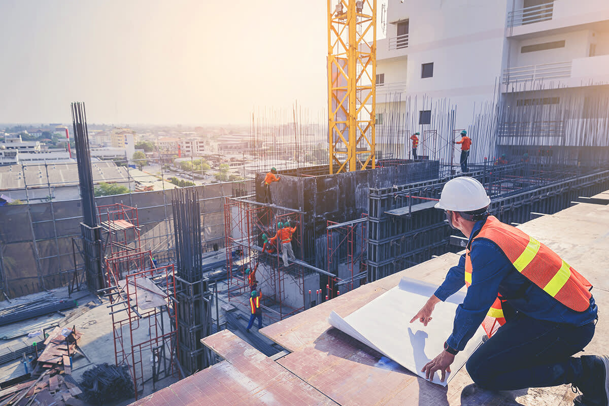 Structural engineer and architect working with blueprints discuss at the outdoors construction site.