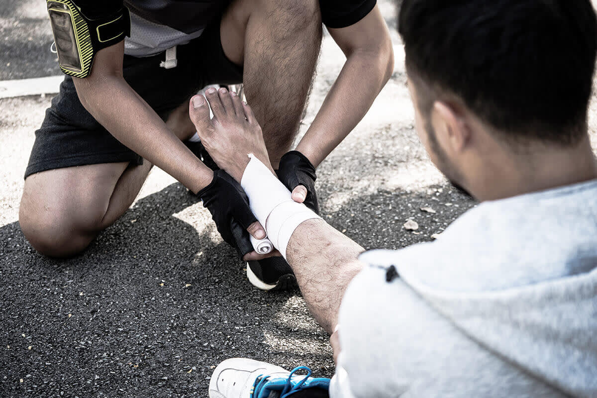 A man uses elastic bandage for pain relief one man's ankle after a workout in a park.