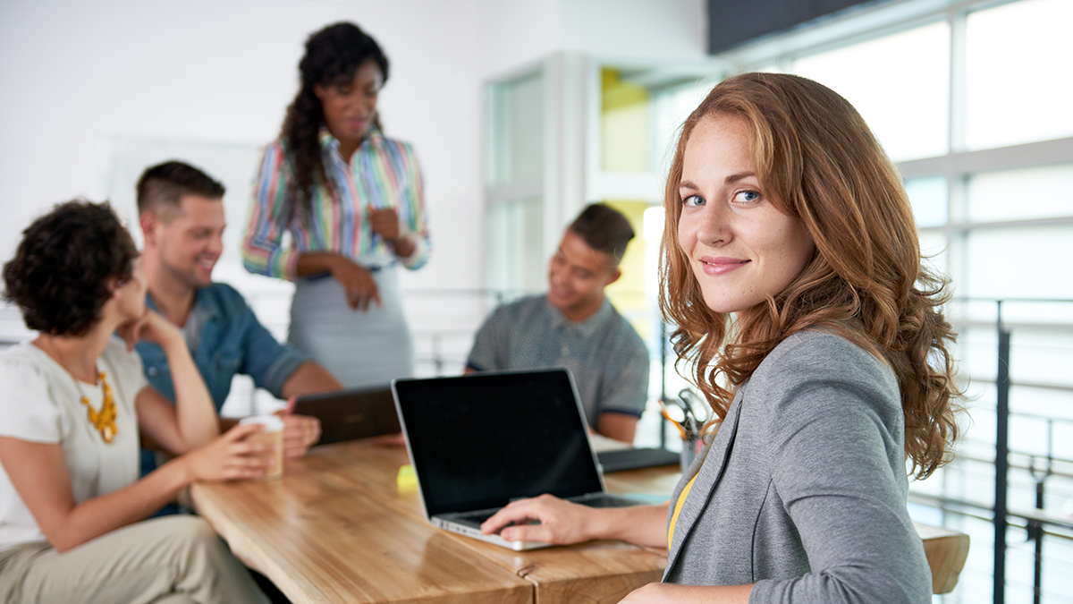 A woman in a meeting looking back from her laptop.