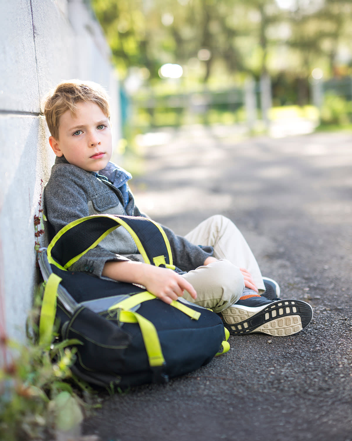 A boy with his backpack sitting on the ground looking sad