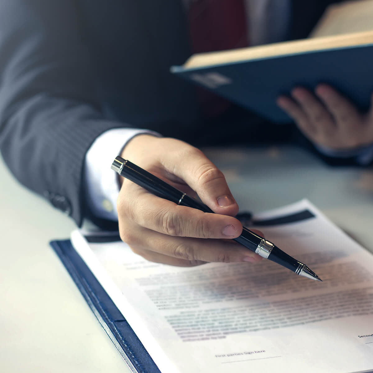Man in suit pointing with pen and holding book