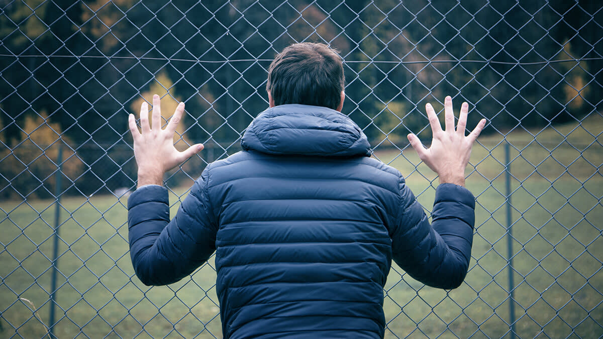 Man with his hands up against the fence looking onward