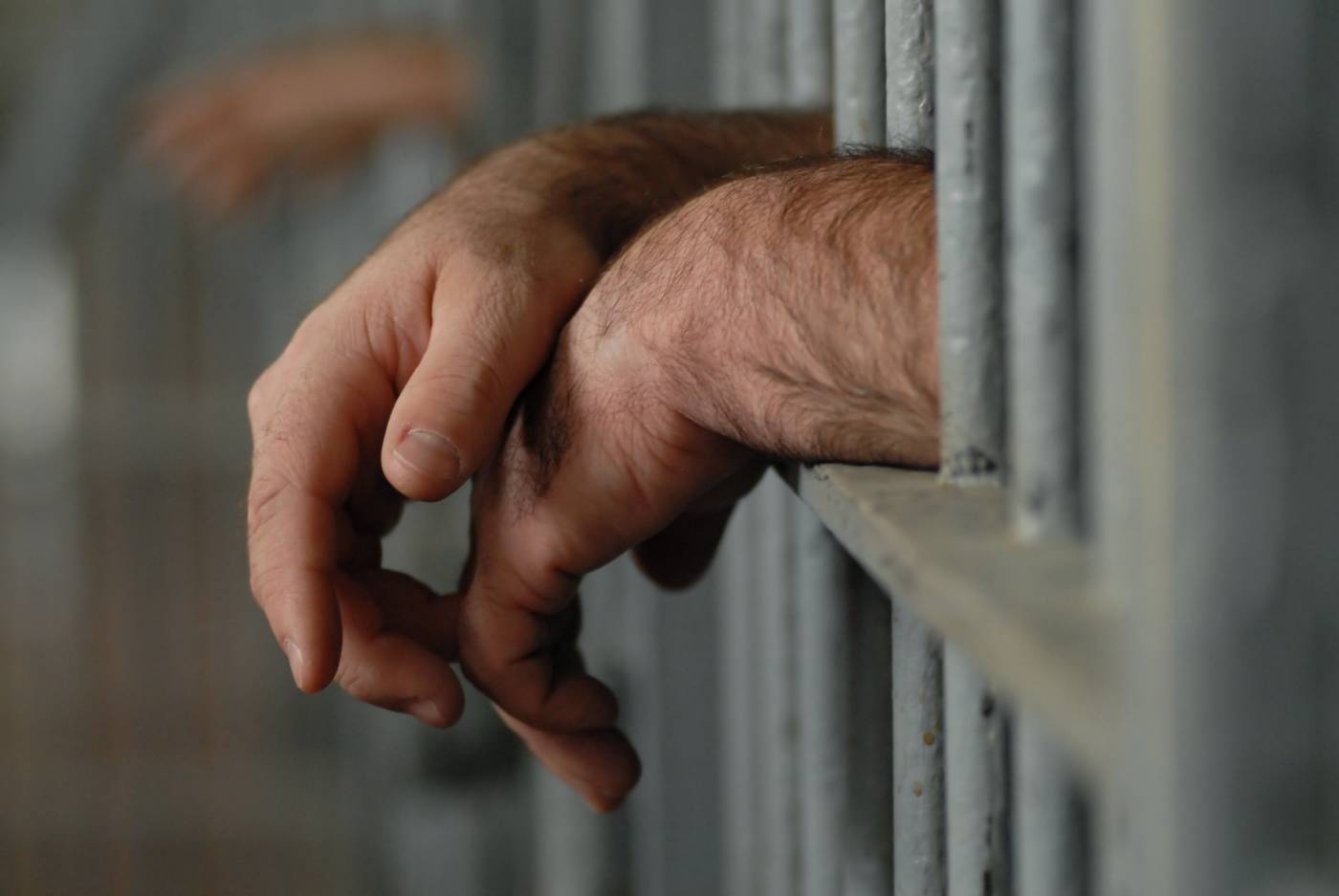 Hands leaning on jail cell bars
