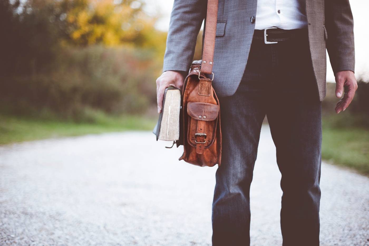 Man walking on road with bag and book in hand