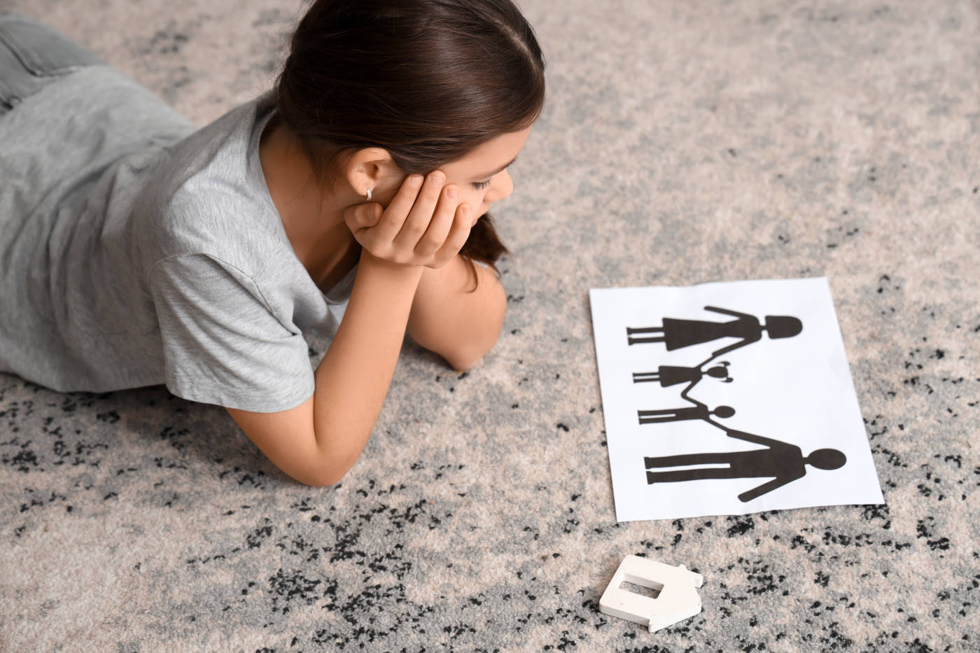 Sad girl with paper family figure lying on carpet