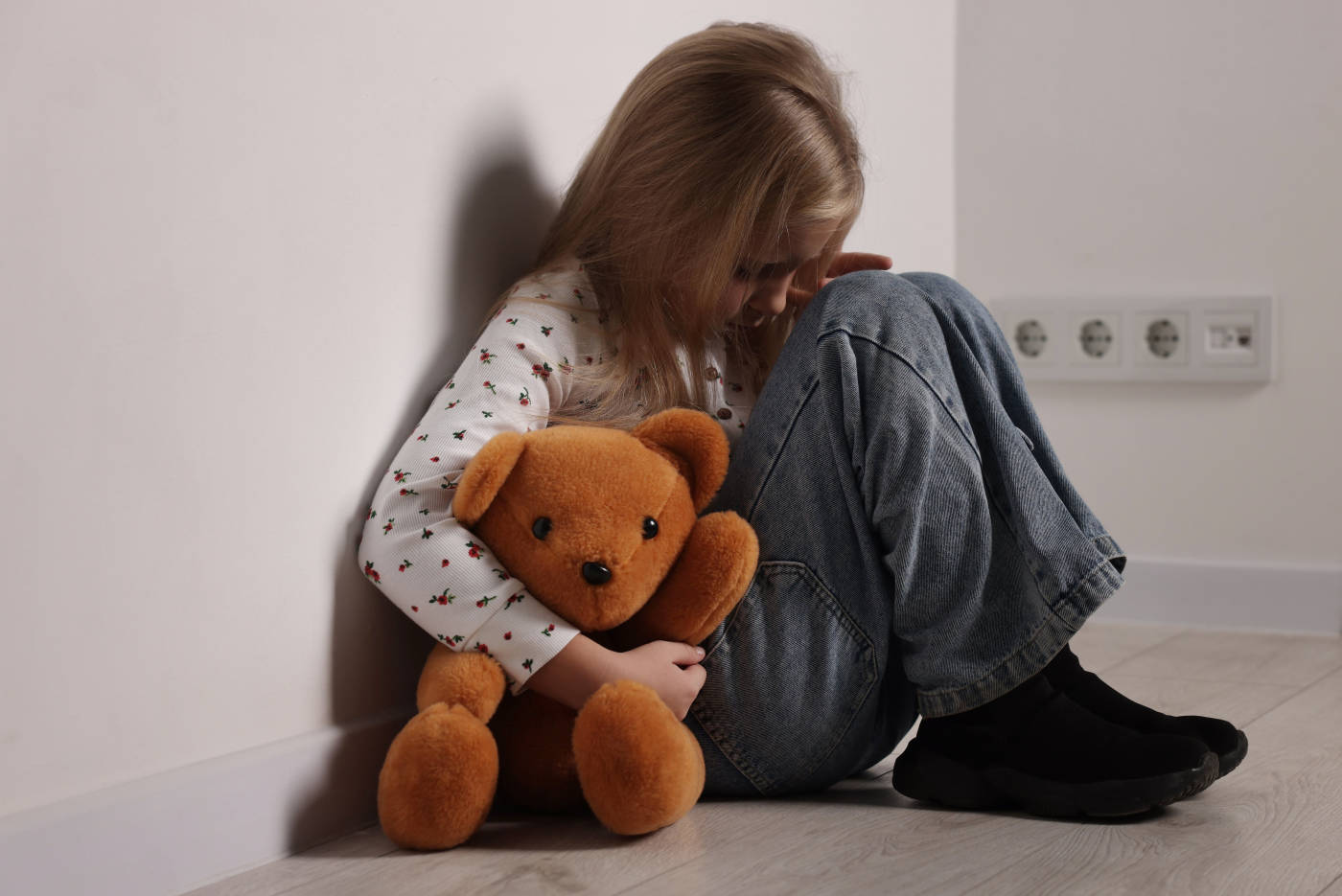 Sad little girl with toy bear near white wall