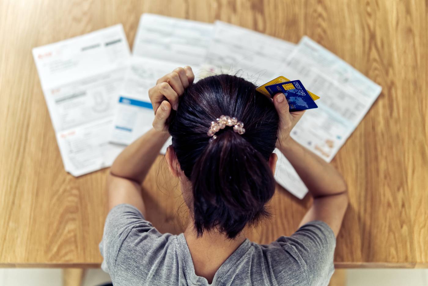 Young woman holding her head in her hands while staring at a stack of credit card bills