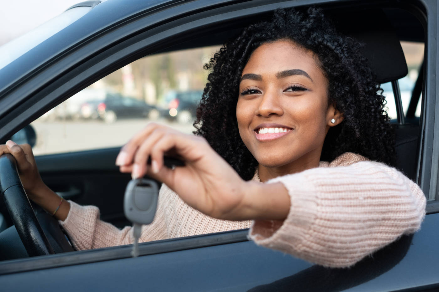 A young woman sits in her car holding car keys
