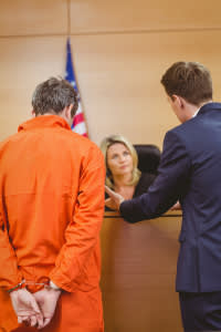 Attorney talking with judge and his client in orange prison suit