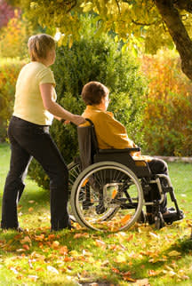 Woman pushing another woman in a wheelchair in the woods