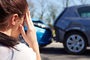 Stressed woman holding her head, looking at a fender bender