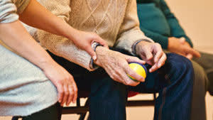 Elderly person sitting down while holding a ball