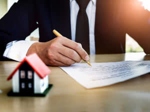 Businessman in suit writing a document with a little house replica nearby