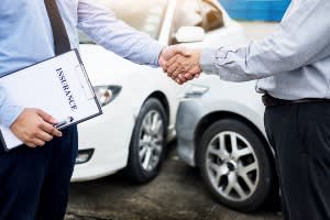 2 men shaking hands with insurance papers in front of a fenderbender 