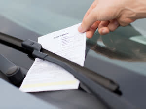 Traffic ticket pinned on a windshield with a hand reaching out to grab it