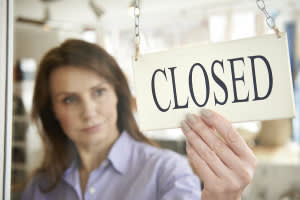 Businesswoman adjusting a sign in a window that says "CLOSED"