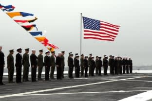 Men and women in uniform standing at attention in front of an American flag