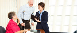 Elderly man on crutches with woman touching his arm both speaking to woman in suit with a clipboard