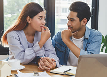 A couple nervously holds hands in front of a laptop