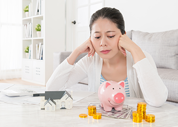 A woman stares at her piggy bank surrounded by money
