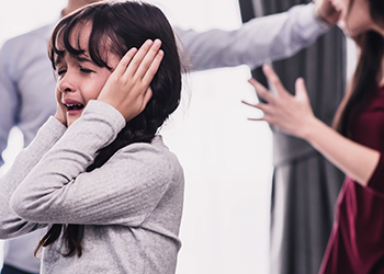 A small girl cries while her parents argue in the background