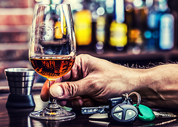 A man holds a whiskey glass next to car keys at a bar