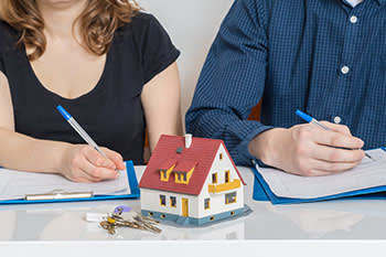 Man and woman filling out divorce paperwork with a house and keys in front of them