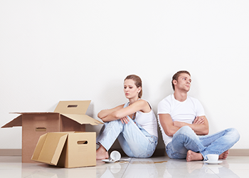 A frustrated couple sits near empty moving boxes