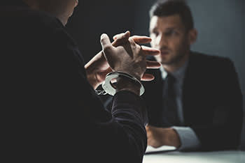 Man in handcuffs speaking to a man in a suit