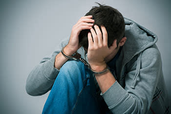 Teenage boy with handcuffs on with his head in his hands