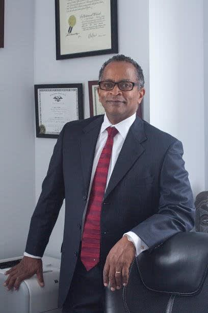 Attorney Jeffrey A. St. Clair leaning against a chair, smiling, in his office. Standing in front of plaques.