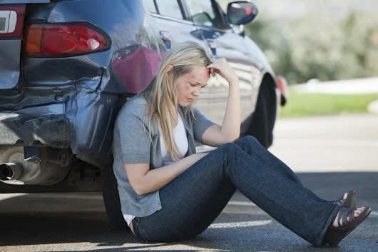 woman with hand on her face sitting next to car