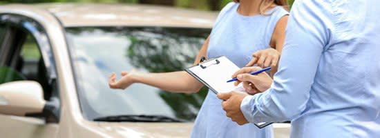 Man writing on a clipboard while woman explains car damage