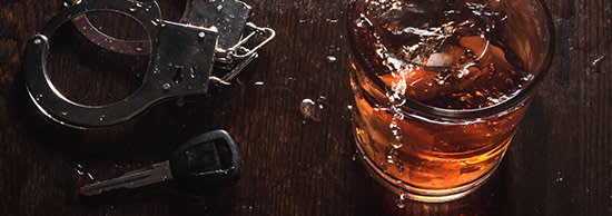 An alcoholic beverage sits next to handcuffs and car keys