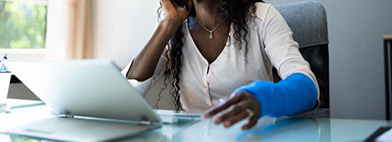 A woman with a broken arm sits at her computer